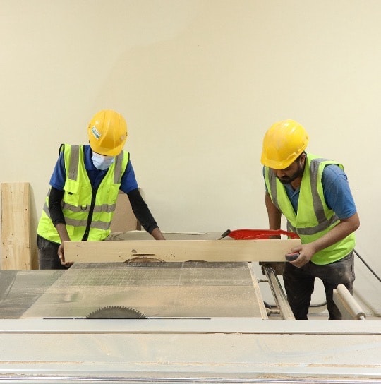 Two craftsmen feeding timber through a table saw